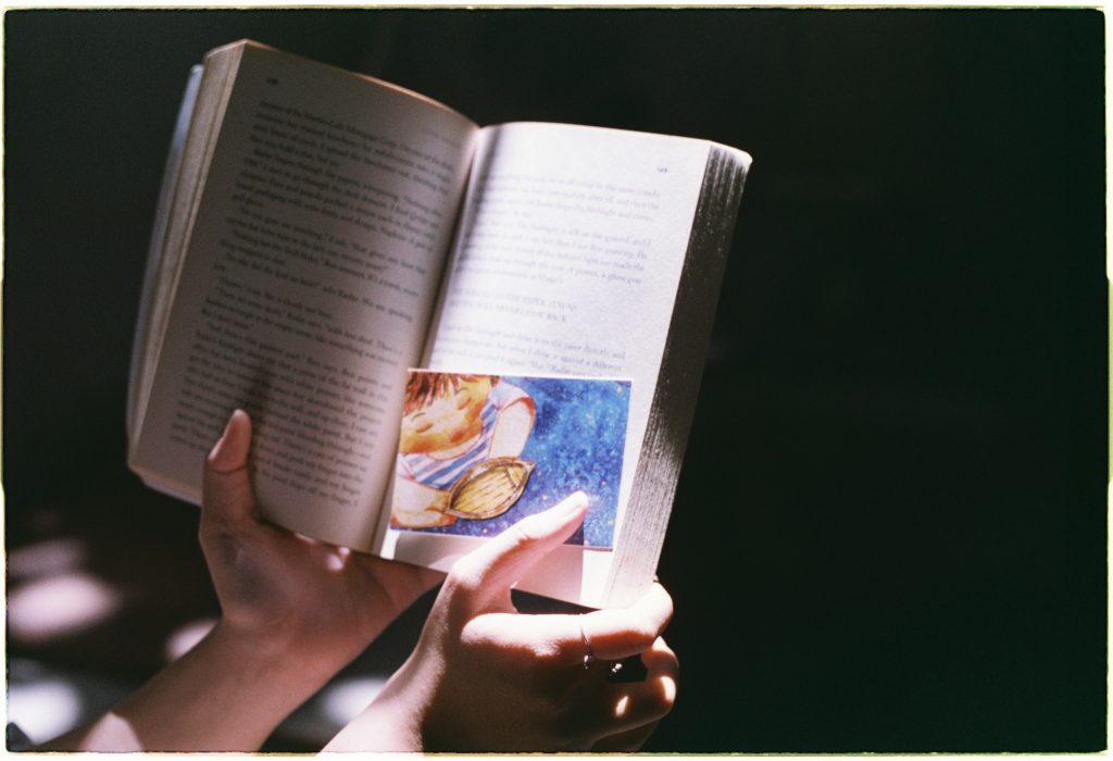 Close-up of hands holding an open book with a colorful illustration inserted, evoking a love for reading.
